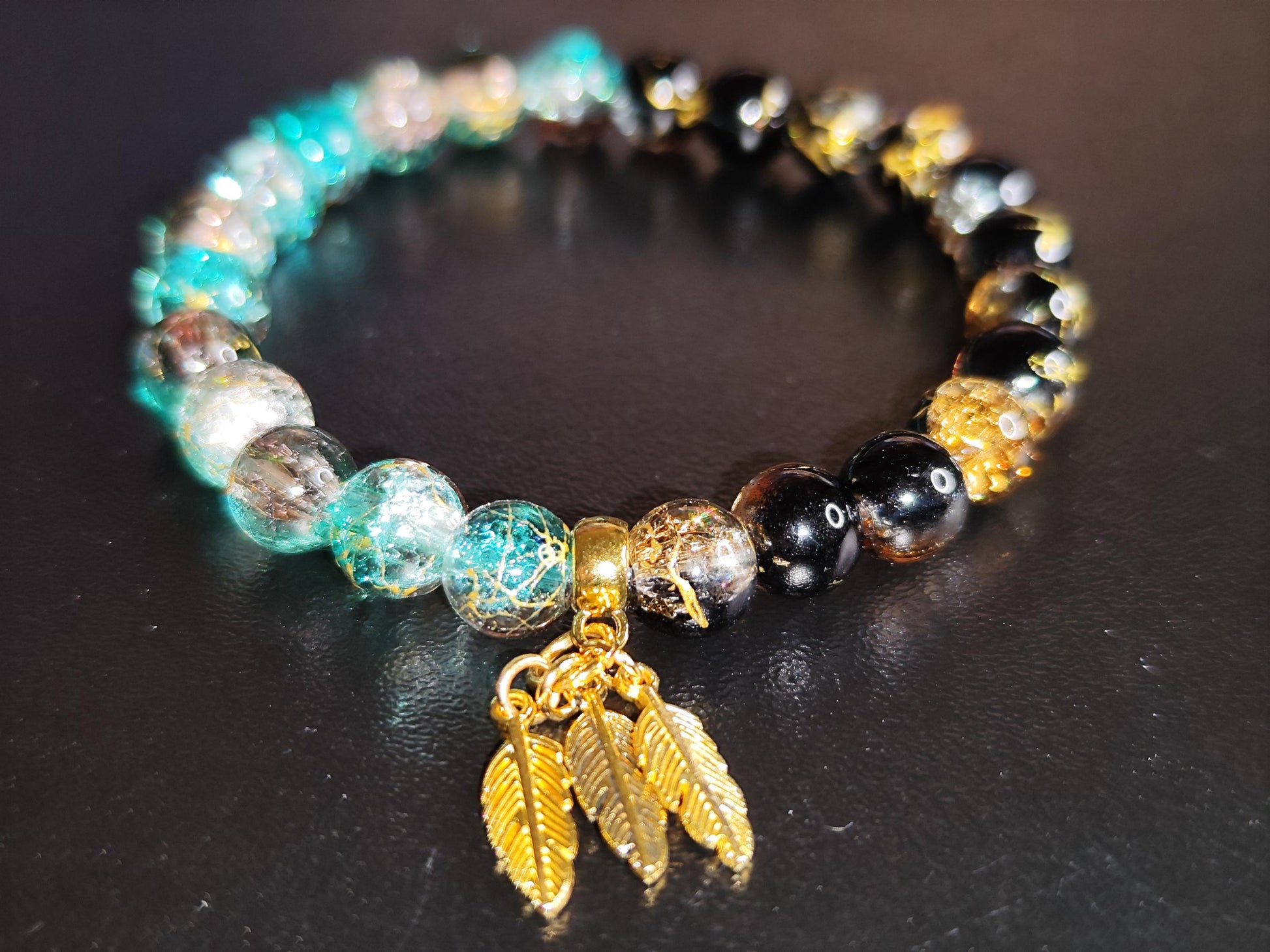 Handgemachtes Armband aus schimmernden Glasperlen mit goldfarbenen Feder-Anhängern – Boho Schmuck – Geschenk für Frauen – Elastisches Armban